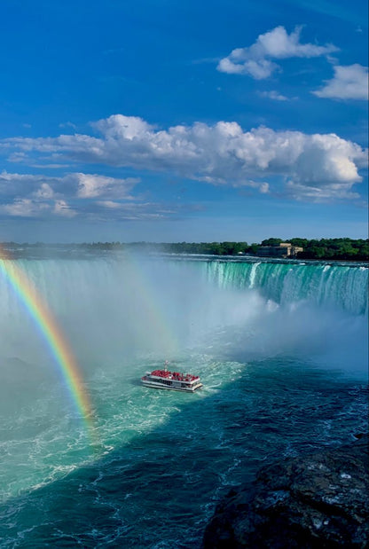 Niagara Falls with a rainbow and a tour boat under a blue sky.