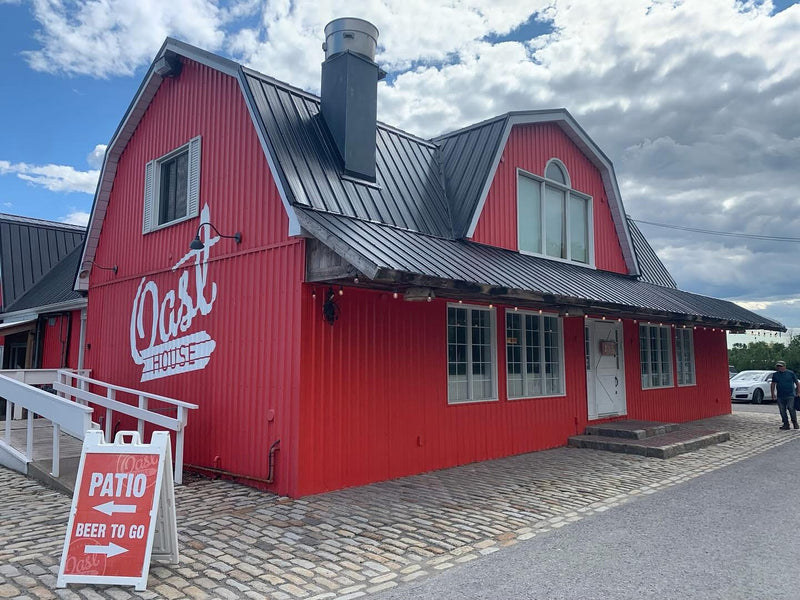 Red building with 'Oast House' sign and outdoor seating sign on a cloudy day.