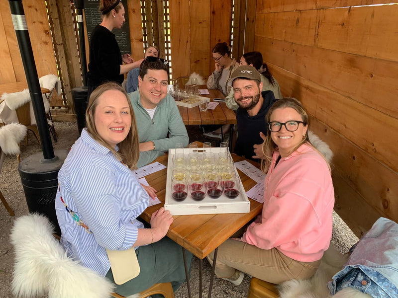 Group of people sitting around a table with wine glasses in a cozy indoor setting.