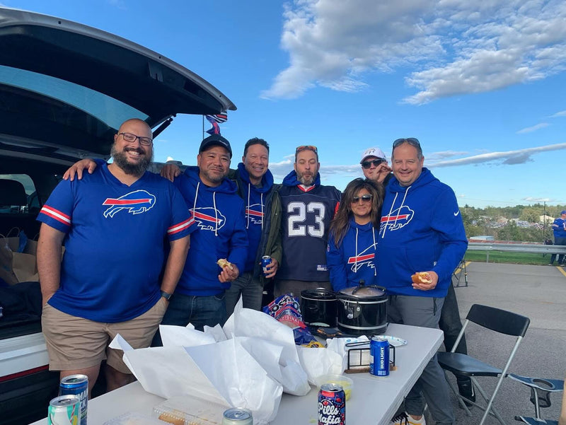 Group of people in blue sports team gear posing outdoors with a table of food and drinks.