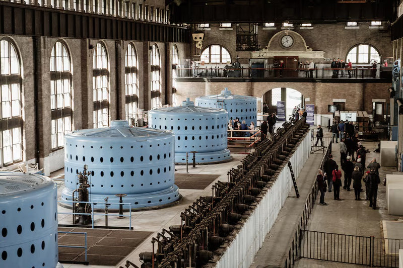 Large industrial interior with blue cylindrical structures and people walking around.