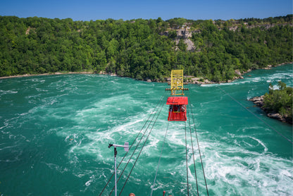 Red cable car over a turbulent river with green cliffs in the background