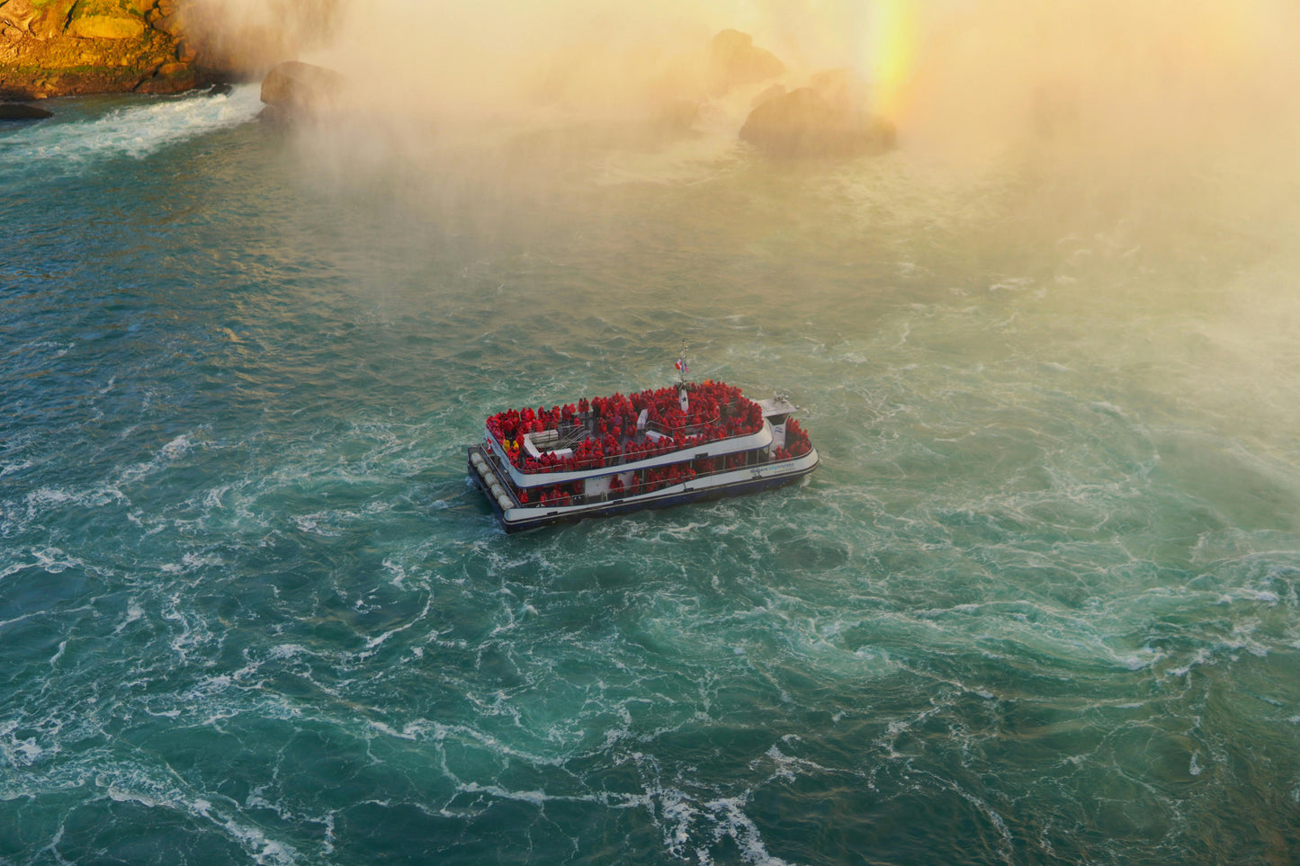 Tourist boat in front of a waterfall with mist and blue-green water.