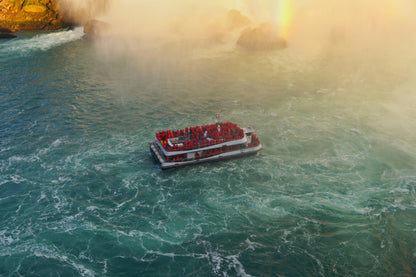 Tourist boat in front of a waterfall with mist and blue-green water.